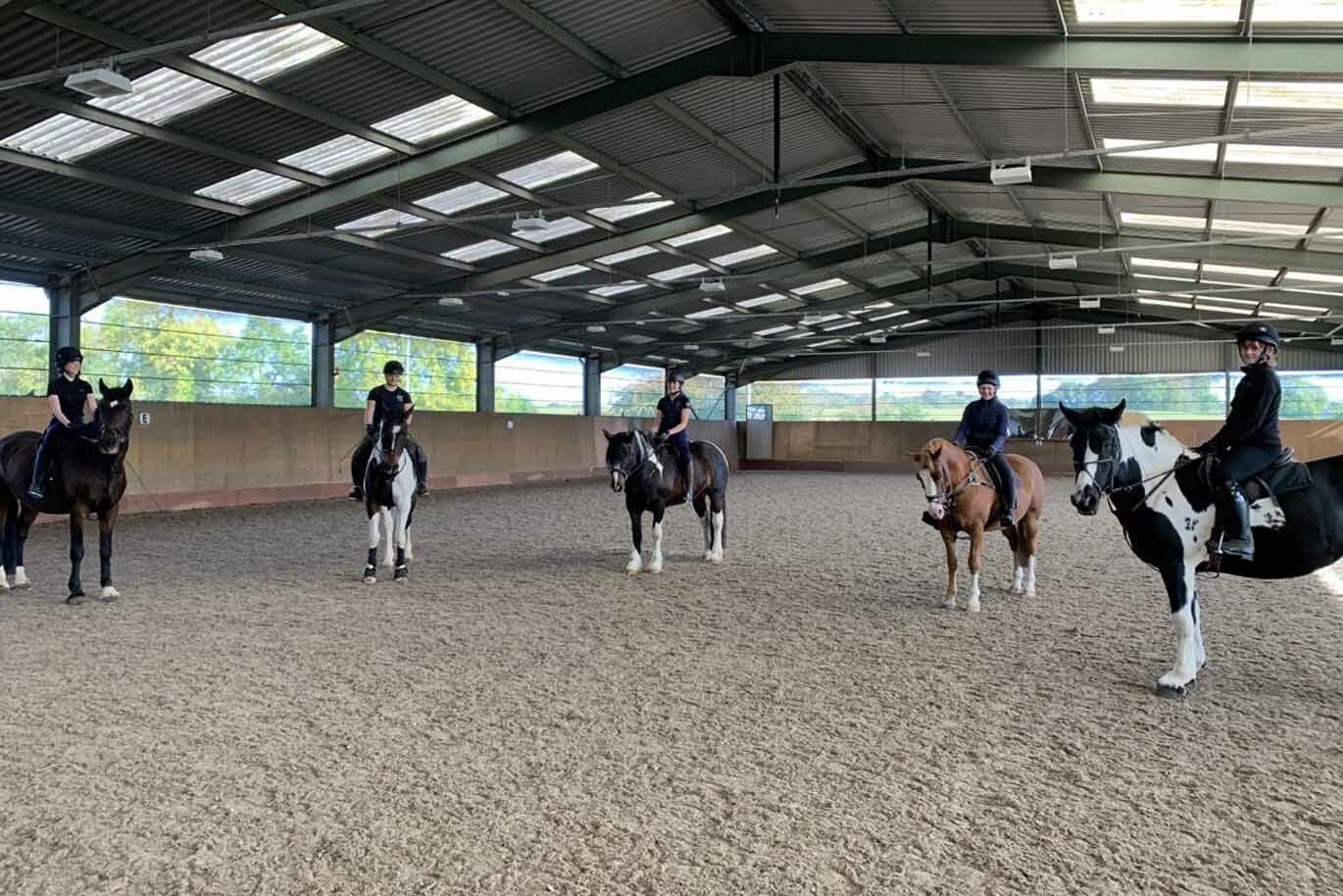 Equine students smiling on horseback indoor arena