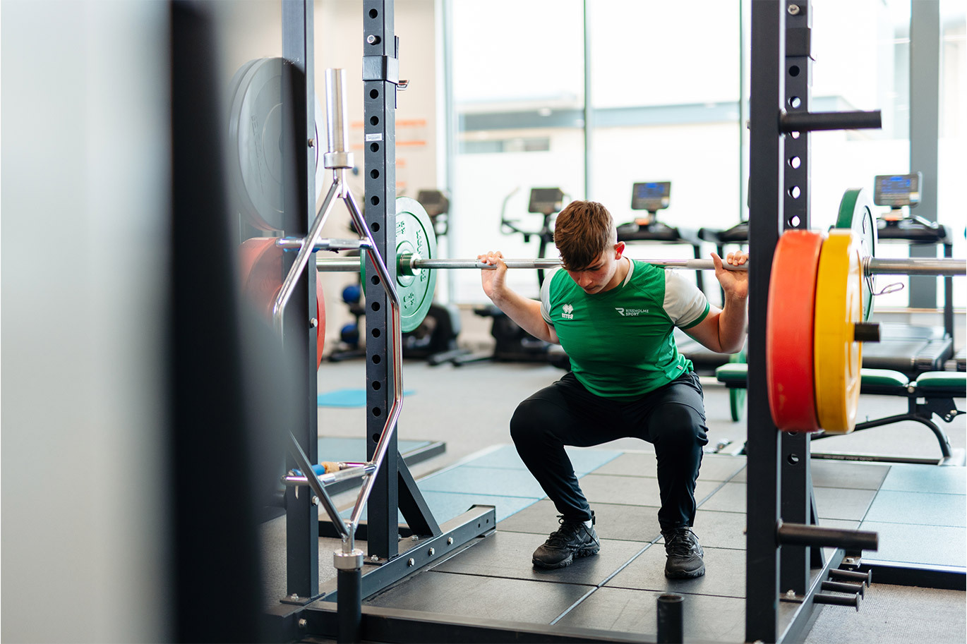 Male sports student squating with weights in onsite gym